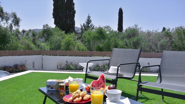 A breakfast setup on a patio with a table, chairs, and a view of greenery and trees. - Villa Bratou Terra (Corfu)