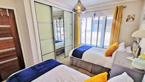 A hotel room with two beds, a sliding glass door, a bedside table with a lamp, and a view of the city through large windows. - Contemporary retreat with fantastic views, hot tub and large garden  (Narberth)