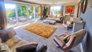 A spacious living room with a large window, a grey sofa set, a brown rug, and a ceiling fan. - Contemporary retreat with fantastic views, hot tub and large garden  (Narberth)