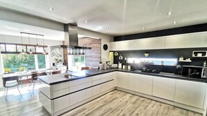 A modern kitchen with a large island, white cabinetry, and a view of greenery outside. - Contemporary retreat with fantastic views, hot tub and large garden  (Narberth)