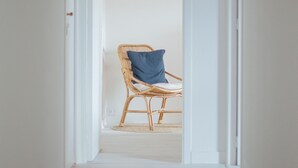A narrow hallway with a wooden floor leading to a room with a wicker chair and a blue pillow. - A stone's throw from the beaches, house with large enclosed garden (Cléder)