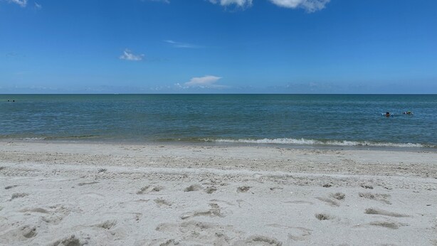 Une plage où l’on peut voir des empreintes de pas dans le sable, sous un ciel bleu et dégagé.