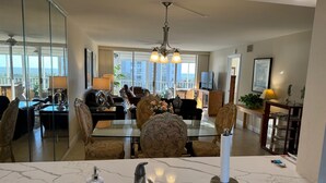 Un salon moderne avec une table à manger en verre, des sièges confortables, un lustre et une vue sur l’extérieur.