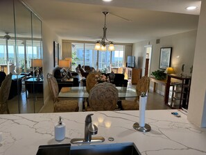 Uma sala de estar moderna com uma mesa de jantar de vidro, assentos confortáveis, um lustre e vista para o exterior.