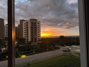 Vista de um edifício de vários andares com telhado curvo, rodeado por vegetação e uma rua com postes de iluminação.