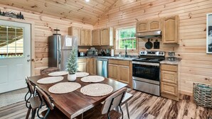 Una cucina in stile baita, con tavolo da pranzo, mobili in legno, elettrodomestici in acciaio inossidabile e vista sull'esterno.