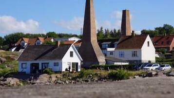 A coastal village with traditional houses, two prominent chimneys, and parked cars.