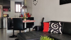 A modern living room with a black leather sofa, a dining table with chairs, and a kitchen area in the background. - OASIS BEACH apartments (Torrevieja)