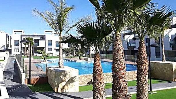 A modern hotel with a swimming pool, palm trees, and a clear blue sky. - OASIS BEACH apartments (Torrevieja)