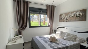 A bedroom with a bed, curtains, a window, a painting, and a bedside table. - OASIS BEACH apartments (Torrevieja)