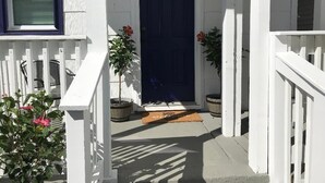 Una casa bianca con una porta blu scuro, ringhiere bianche e piante in vaso.