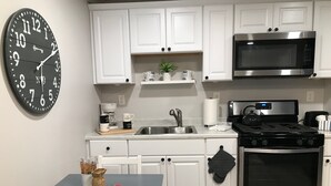 Una cucina moderna con mobili bianchi, un piano cottura in acciaio inossidabile, un forno a microonde e una sveglia nera.