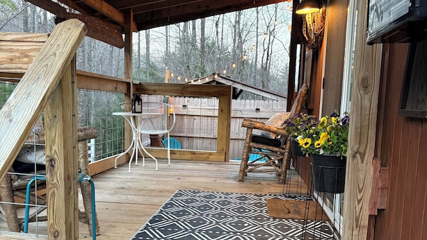 Eine Holzterrasse mit einem gemusterten Teppich, einer Sitzbank und einem hängenden Blumentopf.