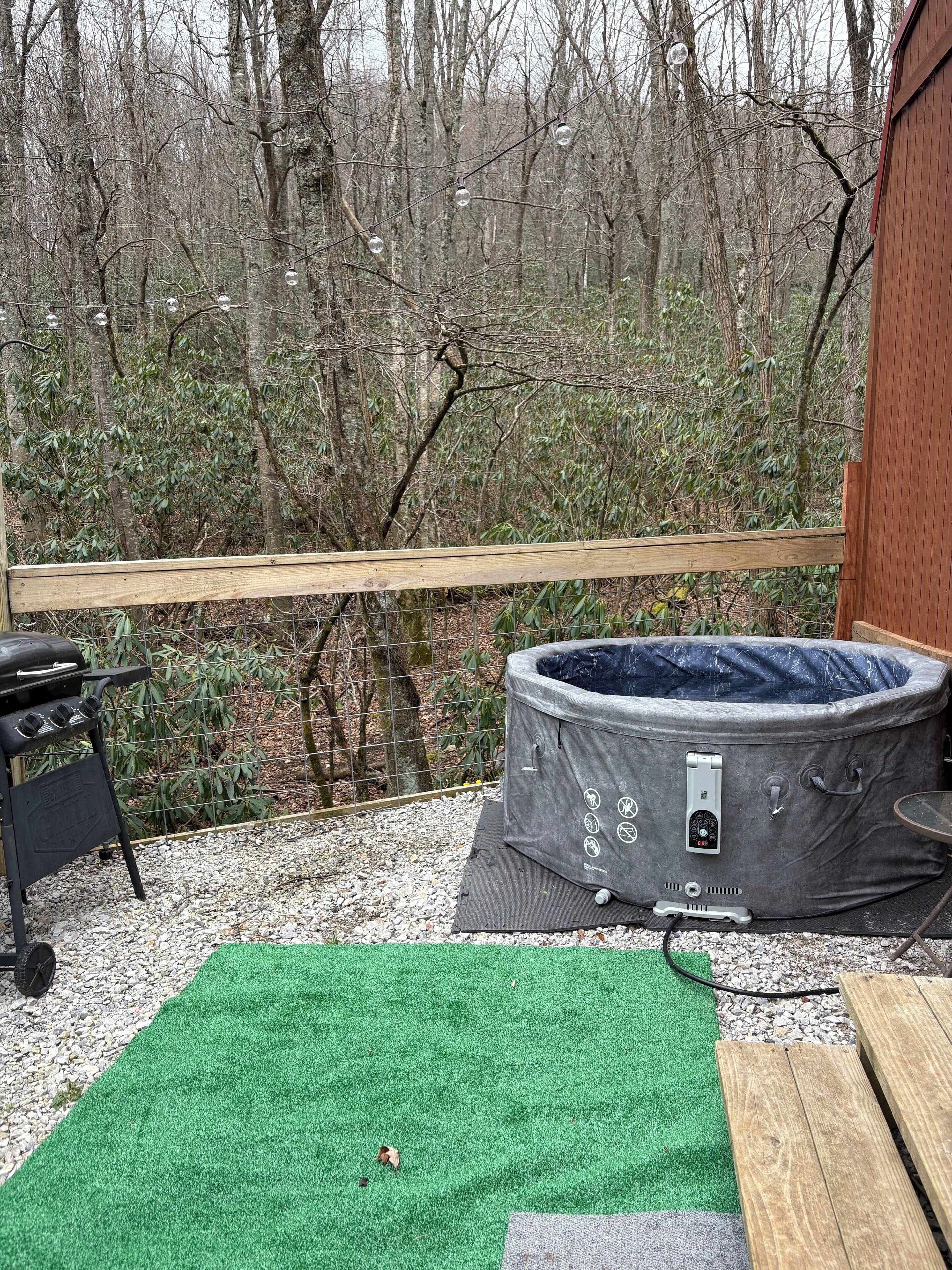 Un jacuzzi en una terraza con barandilla de madera, rodeado de árboles.