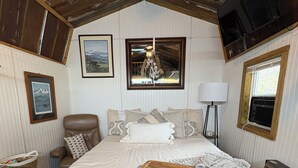 Ein gemütliches Schlafzimmer mit einem großen Bett, einem Holz-Kopfteil, einem Nachttisch mit Lampe und einem gerahmten Bild an der Wand.