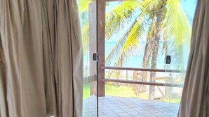 Una stanza con un letto, vista su palme e spiaggia attraverso una porta vetrata.