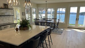 Una cocina amplia con una isla grande, taburetes de bar modernos y vistas a un lago a través de amplios ventanales.