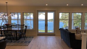 Una habitación amplia con zona de comedor, un sofá y grandes ventanales con vistas a un lago.
