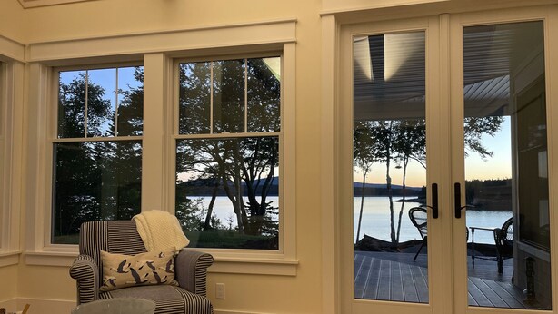 Una habitación con vistas a un lago, una silla con tapicería a rayas y una puerta que da a una terraza al aire libre.