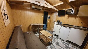 Ett kompakt kök med en inbyggd ugn, en mikrovågsugn och ett handfat. Här finns en träbänk och ett litet runt bord.
