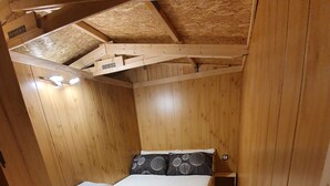 Ett litet sovrum inrett som en enkel stuga, med en säng, två kuddar och en mönstrad matta.