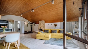Un grand espace de vie avec un canapé jaune, une table à manger avec des chaises, et une cuisine en arrière-plan.