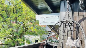 Un fauteuil suspendu avec des coussins, placé sur un balcon offrant une vue sur les arbres et les bâtiments.