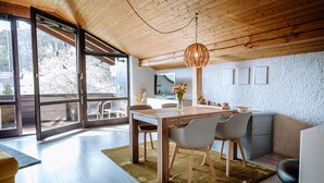Une cuisine moderne avec un plafond en bois, de grandes fenêtres et un coin repas comprenant une table et des chaises.