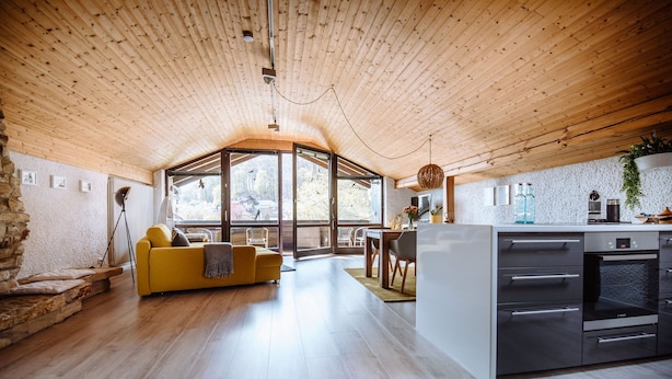 Un vaste espace de vie doté d’un plafond en bois, d’un canapé jaune, d’une table à manger et d’une cuisine équipée d’appareils électroménagers modernes.