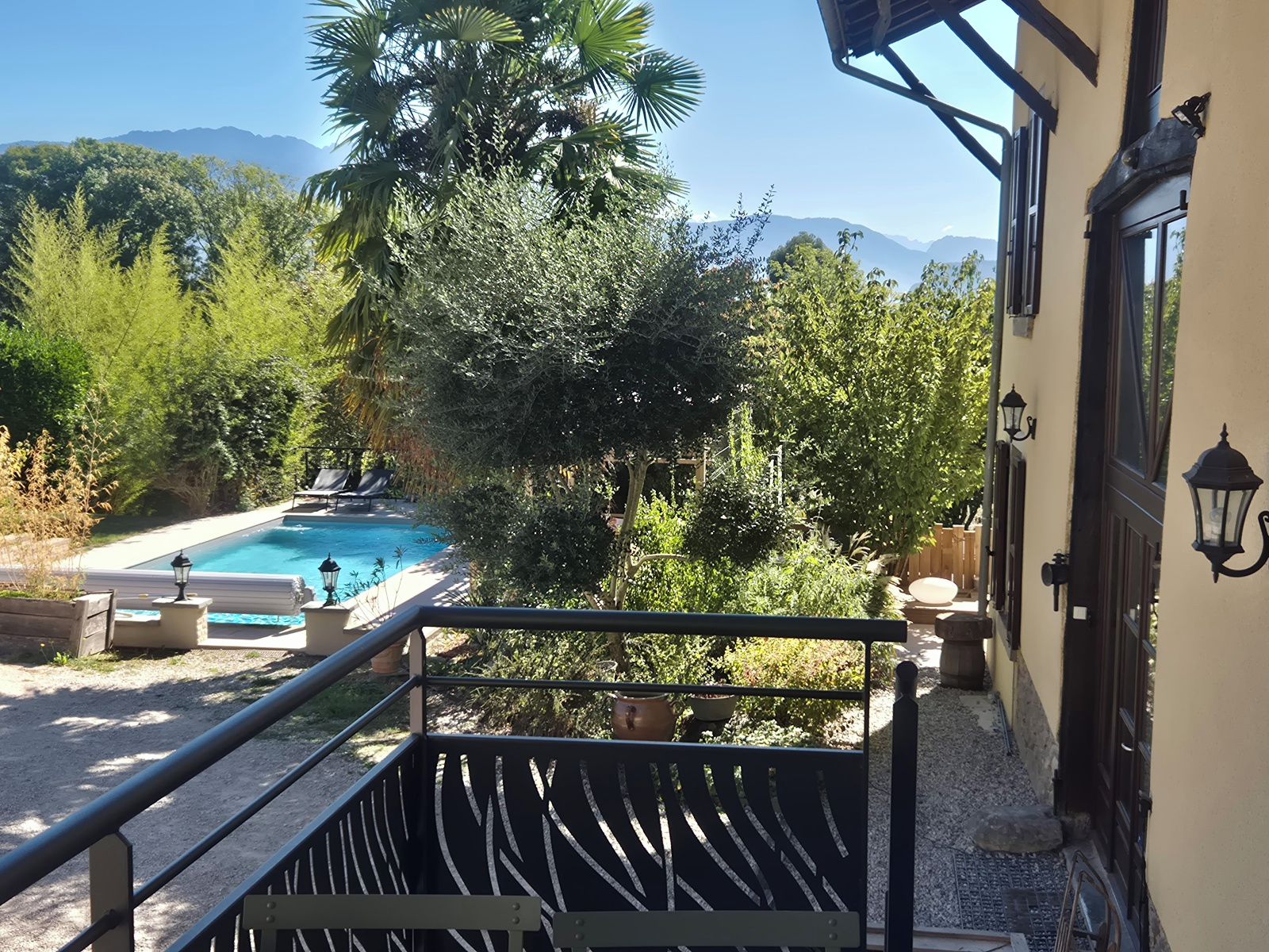 A pool area with a view of mountains, surrounded by lush greenery and a building with a balcony.