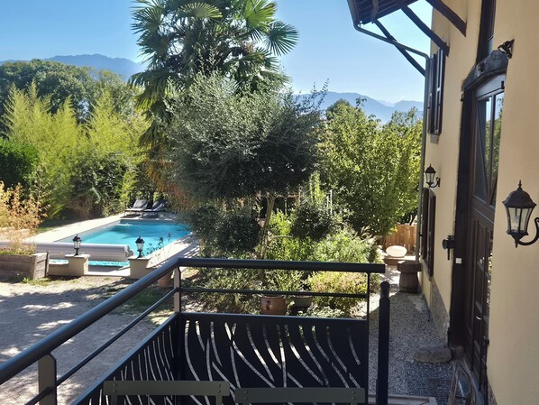 A pool area with a view of mountains, surrounded by lush greenery and a building with a balcony.
