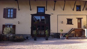 A rustic building with a large wooden door, multiple windows with shutters, and a stone wall foundation.
