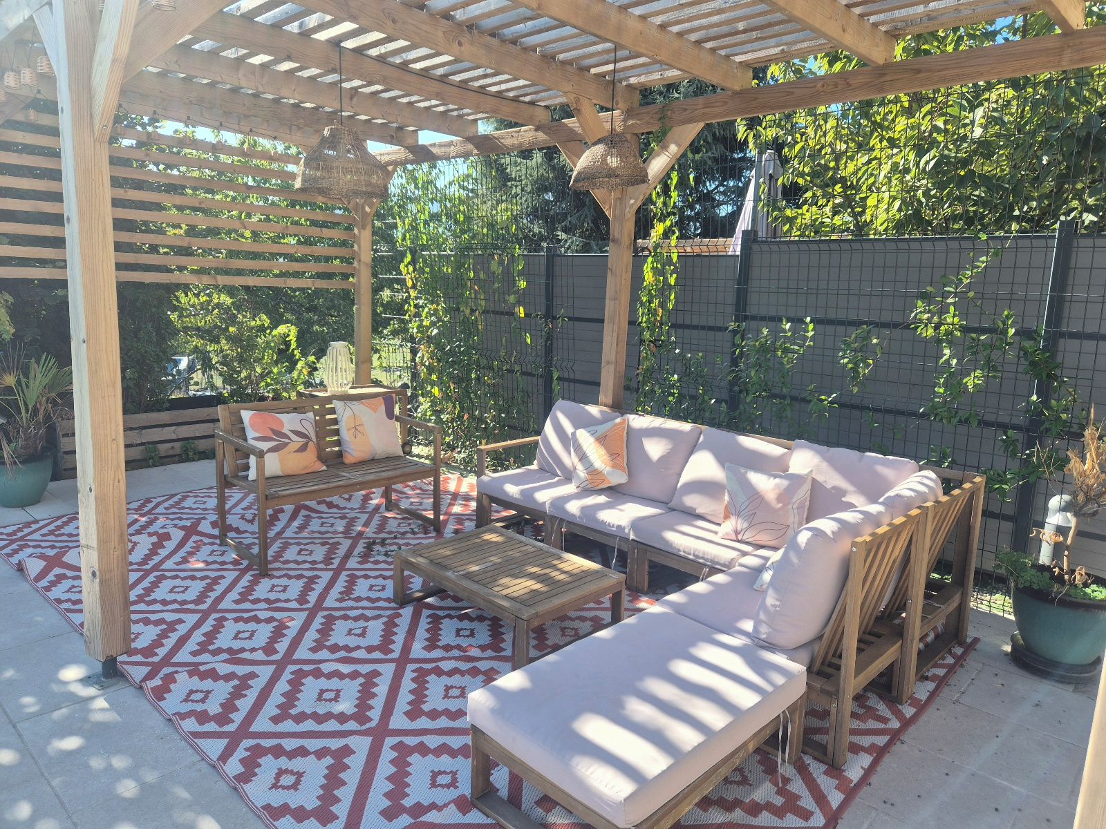 An outdoor patio with a wooden pergola, cushioned seating, and patterned rugs.