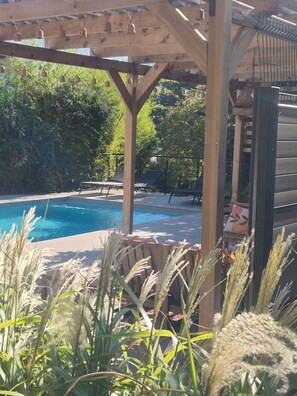 A wooden pergola with hanging lights, a pool, lounge chairs, and a view of a lush garden. - Gîte le Clos D'olon swimming pool & moutain view (Charnècles)
