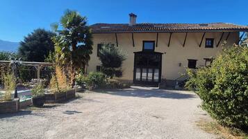 A building with a gravel driveway leading to a gated entrance, surrounded by greenery and a clear sky.