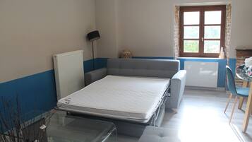 A compact room with a bed, a small table, a chair, a radiator, and a window with curtains.