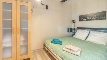 A bedroom with a bed, a wardrobe, a cityscape painting, and a wall-mounted light.