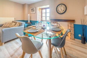 A dining area with a glass table, four chairs, and a clock on the wall.