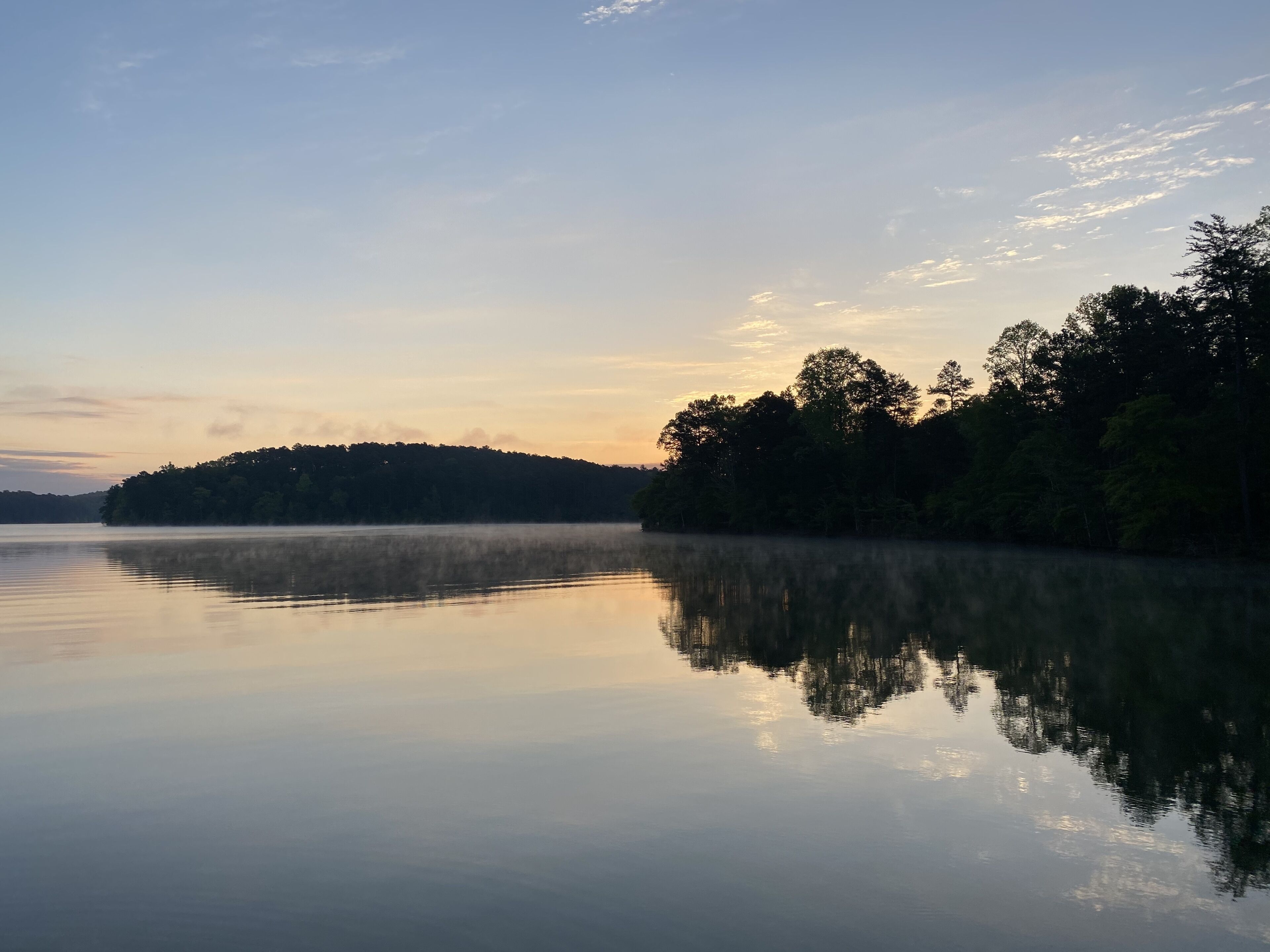 A calm lake with a misty forested island in the distance.