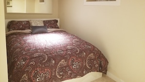 A bedroom with a large bed, a mirror, and a small window with a flower vase. - Basement Suite on Osborne (Winnipeg)