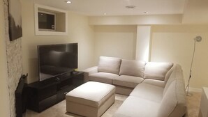 A modern living room with a sectional sofa, a flat-screen TV, and a small window. - Basement Suite on Osborne (Winnipeg)