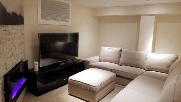 A modern living room with a flat-screen TV, a sofa, and a small ottoman. - Basement Suite on Osborne (Winnipeg)