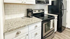 A kitchen with white cabinets, a black microwave, a stainless steel stove, and a black refrigerator. - Downtown Greenville, SC Southern Simplicity! (Greenville)