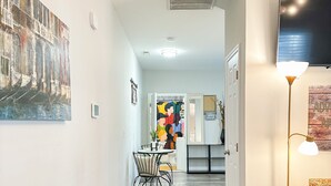 A hallway with a dining area, a blue chair, and a TV mounted on the wall. - Downtown Greenville, SC Southern Simplicity! (Greenville)