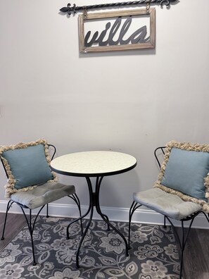 A small round table with two chairs, each with a cushion and a decorative frame. A sign with the word 'villa' hangs above the table.