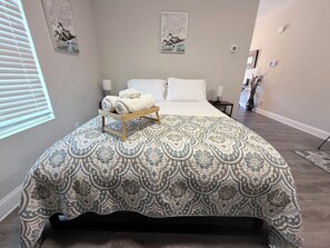 A bedroom with a patterned bedspread, a bedside table with a lamp, and artwork on the walls.