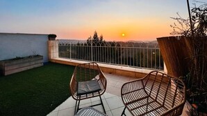 Un balcón con dos sillones de mimbre, vistas al atardecer y barandal blanco.
