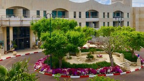 Un edificio moderno con fachada curva, varios balcones y un jardín ajardinado con diversas plantas y flores.