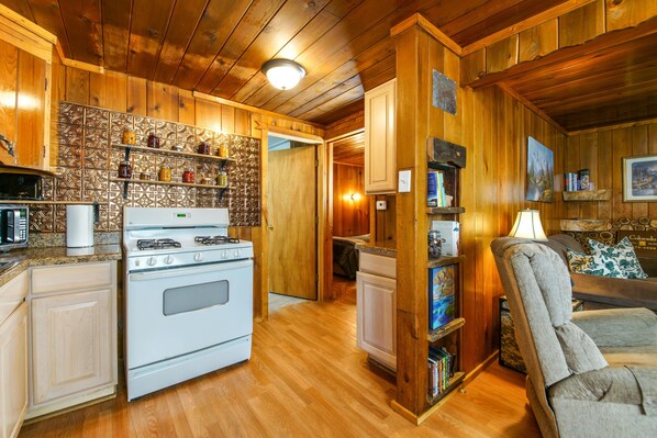 A wooden interior with a kitchen area featuring a stove, microwave, and shelves with jars. - It's time for fall colors, stay in this cabin in the woods. (Bayfield)