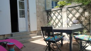 An outdoor patio with a table and chairs, a stone wall, and a wooden door. - Louise's house (Fontenay-le-Comte)